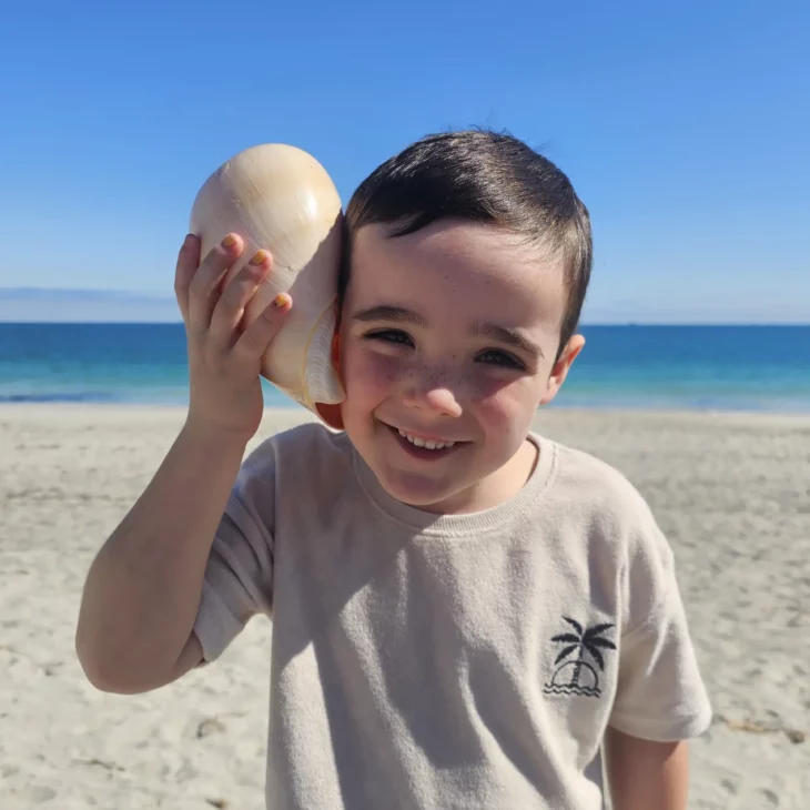 a young boy is holding a large shell up to his ear