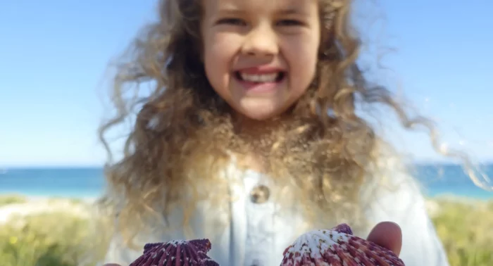 a young girl holds two shells in her out stretched hands